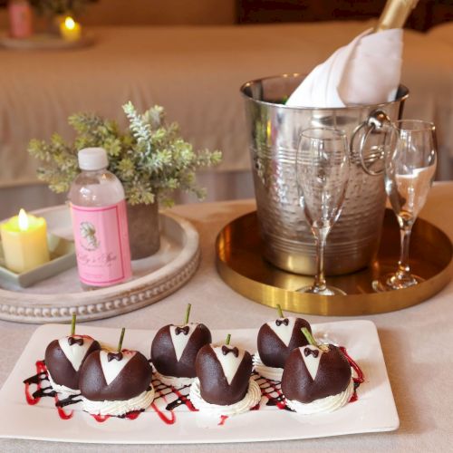 Chocolates on a white plate with dessert drizzle, a candlelit table setup, and a champagne bucket with glasses in a cozy spa-like setting.