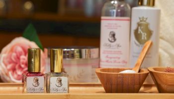 A vanity table with small perfume bottles, wooden bowls with spoons, a pink rose, and taller bottles in the background.