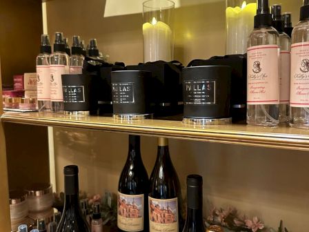 A shelf of beauty products with jars, bottles, and candles, including pink labels, black containers, and small spray bottles, arranged on display.